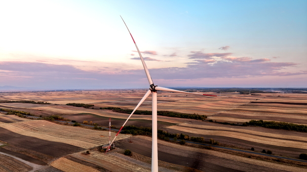 Aerial view of a wind turbine standing in the vast agricultural fields of Vojvodina at sunset with golden harvested land and a soft sky in Vladimirovac Vojvodina Serbia.