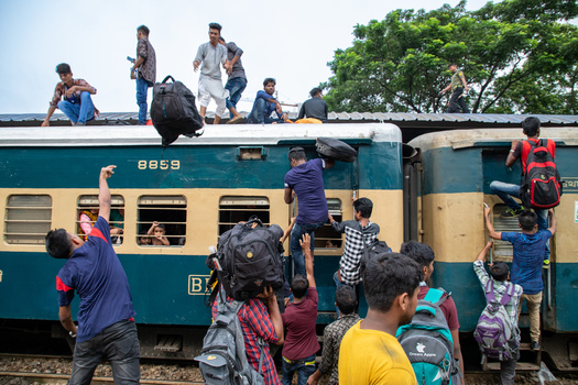 Dhaka Bangladesh 14 June 2018 View of people climbing onto the roof and through windows of a crowded train at Airport Railway Station with green trees in the background. Dhaka Bangladesh 14 June 2018 View of people climbing onto the roof and through windows of a crowded train at Airport Railway Station with green trees in the background.