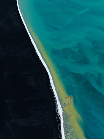 Aerial view of the contrast between black volcanic sand and turquoise glacial water along the coastline of Iceland. Aerial view of the contrast between black volcanic sand and turquoise glacial water along the coastline of Iceland.