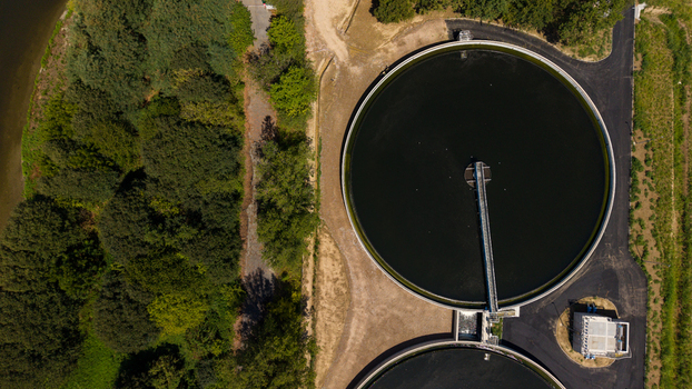 Aerial view of a wastewater treatment plant featuring large circular sedimentation tanks and paved pathways surrounded by dense green vegetation in Milan Lombardy Italy. Aerial view of a wastewater treatment plant featuring large circular sedimentation tanks and paved pathways surrounded by dense green vegetation in Milan Lombardy Italy.