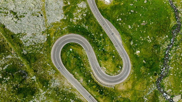 Aerial view of the winding Transfagarasan mountain road cutting through lush green alpine slopes with rocky terrain and a small stream Curtea de Arges Judetul Arges Romania. Aerial view of the winding Transfagarasan mountain road cutting through lush green alpine slopes with rocky terrain and a small stream Curtea de Arges Judetul Arges Romania.