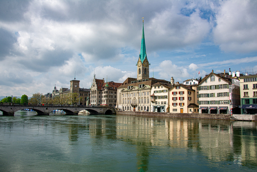 View of the Fraumunster church with its iconic spire rising above historic buildings along the Limmat river in Zurich Zurich Switzerland.