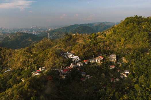 Aerial view of Busay hills and residential houses nestled in lush tropical greenery with the city skyline in the distance Cebu City Central Visayas Philippines.