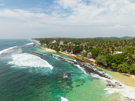 Aerial view of Thalpe Beach featuring turquoise ocean waves crashing on the sandy shoreline and dense palm tree forest in Talpe Southern Province Sri Lanka. Aerial view of Thalpe Beach featuring turquoise ocean waves crashing on the sandy shoreline and dense palm tree forest in Talpe Southern Province Sri Lanka.