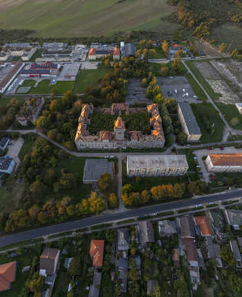 Aerial view of the historic Hajmasker Barracks featuring a prominent central tower and surrounding lush trees set amidst residential buildings and green fields in Hajmasker Hungary. Aerial view of the historic Hajmasker Barracks featuring a prominent central tower and surrounding lush trees set amidst residential buildings and green fields in Hajmasker Hungary.