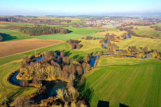 Aerial view of the winding Aisch river flowing through green meadows and autumn trees near the village of Uehlfeld Bayern Germany. Aerial view of the winding Aisch river flowing through green meadows and autumn trees near the village of Uehlfeld Bayern Germany.
