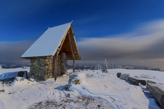 View of a snow covered stone and wood structure atop a hill under a blue sky fading to orange at the horizon a crisp winter scene Schöckl Styria Austria. View of a snow covered stone and wood structure atop a hill under a blue sky fading to orange at the horizon a crisp winter scene Schöckl Styria Austria.