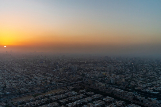 Aerial view of the sprawling cityscape of Karachi at sunset with golden light illuminating the horizon and dense urban development stretching across the landscape in Karachi Sindh Pakistan.