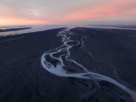 Aerial view of a braided river system carves through the volcanic landscape under a pastel sky in Iceland. Iceland Iceland. Aerial view of a braided river system carves through the volcanic landscape under a pastel sky in Iceland. Iceland Iceland.