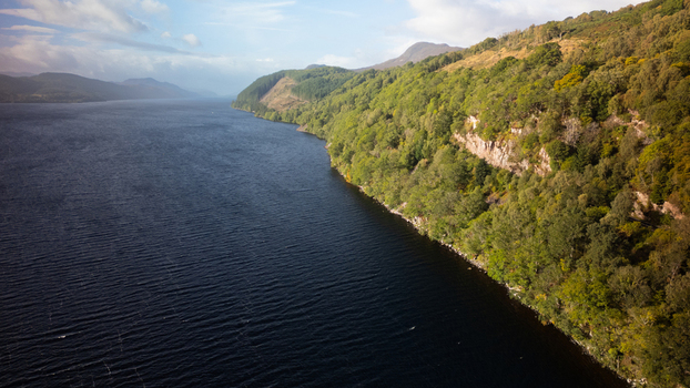 Aerial view of Loch Ness with its deep blue waters bordered by lush green forested hills and rugged cliffs in Highland Council Scotland United Kingdom.