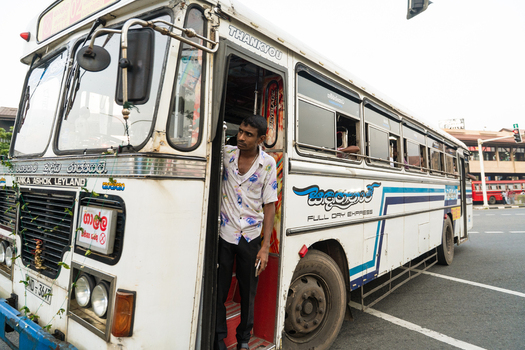 Sri Lanka 15 January 2026 View of a white Lanka Ashok Leyland bus with a man standing in the doorway on a city street.