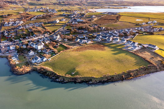 Aerial view of the coastal town featuring green fields houses and rugged coastline along the bay in golden hour light Dunfanaghy County Donegal Ireland. Aerial view of the coastal town featuring green fields houses and rugged coastline along the bay in golden hour light Dunfanaghy County Donegal Ireland.