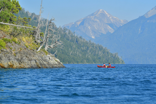 View of two people in a red kayak on the blue waters of Nahuel Huapi Lake with mountains in the background San Carlos de Bariloche Rio Negro Argentina. View of two people in a red kayak on the blue waters of Nahuel Huapi Lake with mountains in the background San Carlos de Bariloche Rio Negro Argentina.