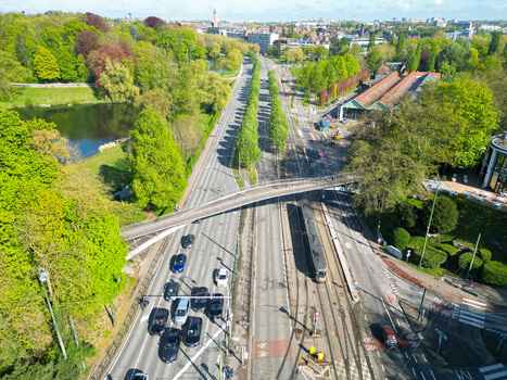 Aerial view of a multi lane road with traffic a tram and a pedestrian bridge surrounded by lush green trees and a park in Woluwe Saint Pierre Bruxelles Belgium. Aerial view of a multi lane road with traffic a tram and a pedestrian bridge surrounded by lush green trees and a park in Woluwe Saint Pierre Bruxelles Belgium.