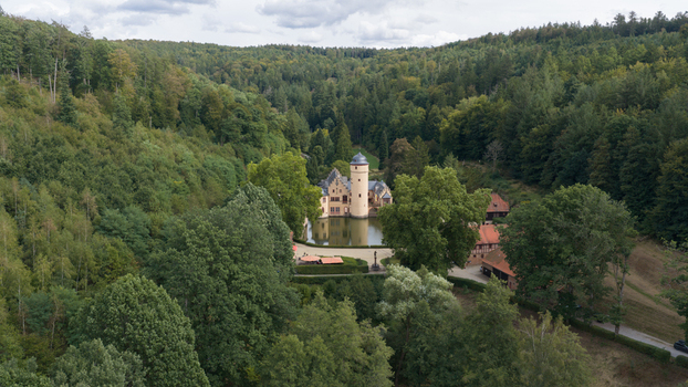 Aerial view of Schloss Mespelbrunn a historic water castle surrounded by dense green forests and a calm pond in Mespelbrunn Bayern Germany.