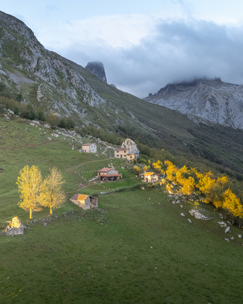 Aerial view of rustic dwellings nestled against the rugged towering peaks of Picos de Europa where golden foliage meets the cool grey stone Picos de Europa Asturias Spain. Aerial view of rustic dwellings nestled against the rugged towering peaks of Picos de Europa where golden foliage meets the cool grey stone Picos de Europa Asturias Spain.