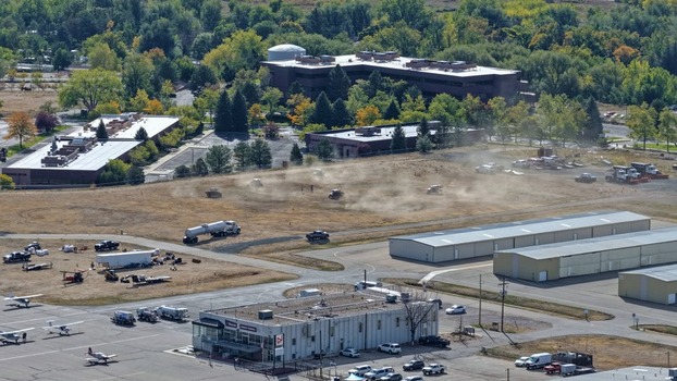 Aerial view of construction equipment working on an open field near the airport with parked small aircraft and commercial buildings in Boulder Colorado United States. Aerial view of construction equipment working on an open field near the airport with parked small aircraft and commercial buildings in Boulder Colorado United States.
