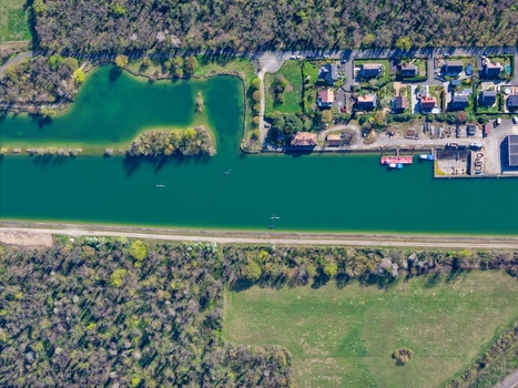 Aerial view of the tranquil canal cutting through the vibrant landscape contrasting with the lush forests and quaint buildings Sausheim Grand Est France.