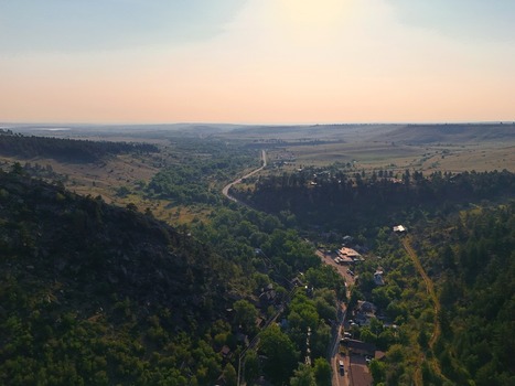 Aerial view of Eldorado Springs canyon with lush green trees a winding road and rocky cliffs under a warm sunset sky in Eldorado Springs Colorado United States.