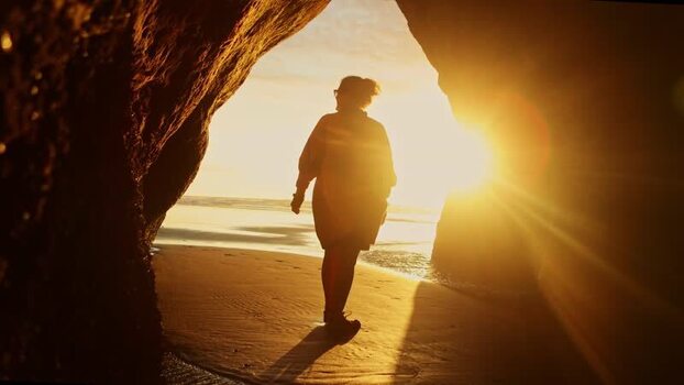 View of a person in a cave opening on a beach New Zealand. View of a person in a cave opening on a beach New Zealand.