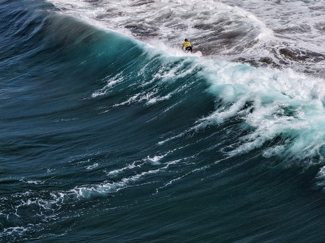 Aerial view of a surfer riding a large turquoise wave with white foam at Praia do Areal de Santa Barbara in Ribeira Grande Acores Portugal. Aerial view of a surfer riding a large turquoise wave with white foam at Praia do Areal de Santa Barbara in Ribeira Grande Acores Portugal.