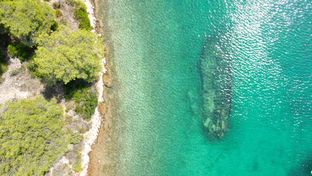 Aerial view of the Kontesa shipwreck submerged in turquoise waters near the rocky coastline and pine trees in Necujam Split Dalmatia County Croatia. Aerial view of the Kontesa shipwreck submerged in turquoise waters near the rocky coastline and pine trees in Necujam Split Dalmatia County Croatia.