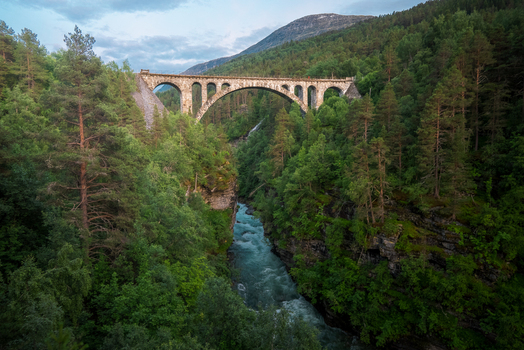View of Kylling Bridge spanning the Rauma River surrounded by dense pine forests and steep rocky terrain in Rauma Municipality More og Romsdal Norway. View of Kylling Bridge spanning the Rauma River surrounded by dense pine forests and steep rocky terrain in Rauma Municipality More og Romsdal Norway.