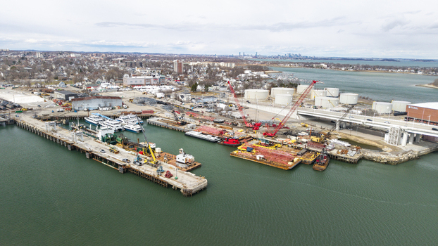 Aerial view of the bustling shipyard filled with vessels and cranes against the backdrop of the distant cityscape Quincy Massachusetts United States.