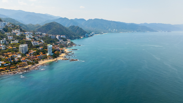 Aerial view of the coastline meeting the ocean buildings nestled amongst the lush hillsides creating a vibrant contrast of urban and natural landscapes Puerto Vallarta Jalisco Mexico.