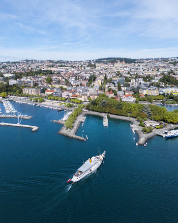 Aerial view of Ouchy Olympique harbor on Lake Geneva with a passenger boat cruising on the blue water surrounded by the cityscape of Lausanne Vaud Switzerland.