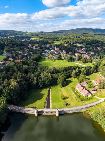 Aerial view of the historic Fojtka Reservoir dam with its stone towers surrounded by lush green forests and the village of Mnisek Liberecky kraj Czechia. Aerial view of the historic Fojtka Reservoir dam with its stone towers surrounded by lush green forests and the village of Mnisek Liberecky kraj Czechia.