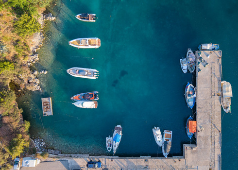 Aerial view of motorboats and fishing vessels moored in the turquoise waters of a small harbor next to a concrete pier in Porto Palermo Qarku i Vlores Albania. Aerial view of motorboats and fishing vessels moored in the turquoise waters of a small harbor next to a concrete pier in Porto Palermo Qarku i Vlores Albania.