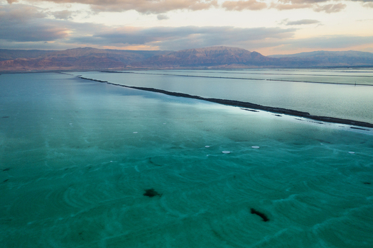 Aerial view of the strikingly vibrant turquoise waters of the Dead Sea contrasting with the deep blues and distant desert mountains under a dramatic sky Ein Bokek Israel. Aerial view of the strikingly vibrant turquoise waters of the Dead Sea contrasting with the deep blues and distant desert mountains under a dramatic sky Ein Bokek Israel.