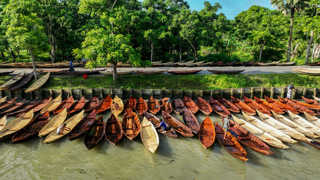Aerial view of wooden boats aligned on the riverbank contrasting with the lush green trees along the road Pirojpur Pourashava Barisal Division Bangladesh. Aerial view of wooden boats aligned on the riverbank contrasting with the lush green trees along the road Pirojpur Pourashava Barisal Division Bangladesh.