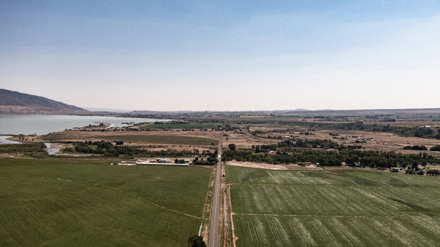 Aerial view of a straight road cutting through green agricultural fields and arid plains leading toward a large lake under a clear sky in Cody Wyoming United States.