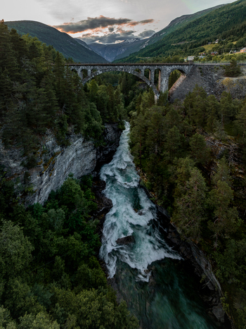 View of Kylling Bridge spanning the rushing Rauma River surrounded by dense pine forests and dramatic mountain peaks in Rauma Municipality More og Romsdal Norway. View of Kylling Bridge spanning the rushing Rauma River surrounded by dense pine forests and dramatic mountain peaks in Rauma Municipality More og Romsdal Norway.