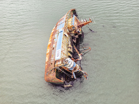 Aerial view of a rusted and partially submerged shipwreck with the identification S 226 on its side in murky coastal waters. Aerial view of a rusted and partially submerged shipwreck with the identification S 226 on its side in murky coastal waters.