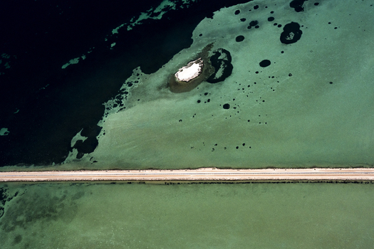 Aerial view of the causeway crossing the shallow turquoise and dark blue waters near Useless Loop showcasing salt mining patterns and a small island in Kalbarri Western Australia Australia. Aerial view of the causeway crossing the shallow turquoise and dark blue waters near Useless Loop showcasing salt mining patterns and a small island in Kalbarri Western Australia Australia.