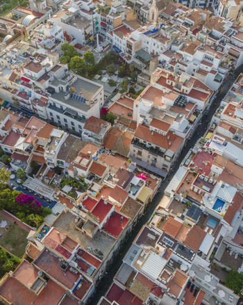 Aerial view of dense terracotta rooftops and narrow streets in the historic center with lush green courtyards in Sitges Catalonia Spain. Aerial view of dense terracotta rooftops and narrow streets in the historic center with lush green courtyards in Sitges Catalonia Spain.