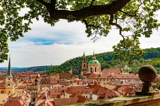 Prague Czechia 08 May 2023 View of St. Nicholas Church rising above historic red tiled rooftops and lush green hills in the city center.
