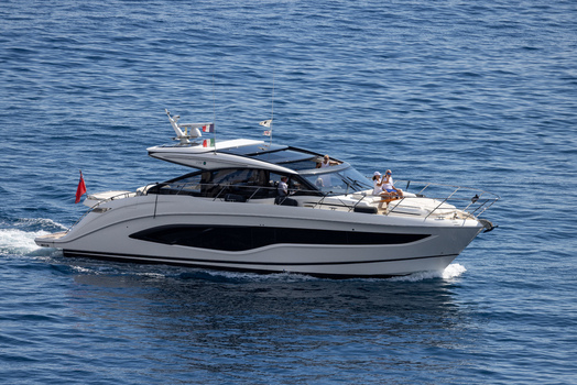 Aerial view of a sleek white motor yacht cruising on the deep blue Mediterranean Sea near the coast of Monaco City with people relaxing on the deck in Monaco Monaco.
