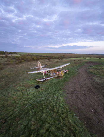 Aerial view of an abandoned graffiti covered biplane resting in a grassy field under a soft sunset sky in Bulgaria. Aerial view of an abandoned graffiti covered biplane resting in a grassy field under a soft sunset sky in Bulgaria.