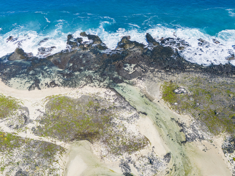 Aerial view of the Kalaemamo coastline featuring dark volcanic rocks crashing turquoise waves and white sandy shores in Hawaii County Hawaii United States. Aerial view of the Kalaemamo coastline featuring dark volcanic rocks crashing turquoise waves and white sandy shores in Hawaii County Hawaii United States.
