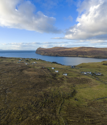 Aerial view of the coastal village of Milovaig with white cottages scattered across the rolling hills overlooking the sea and distant cliffs Milovaig Scotland United Kingdom.