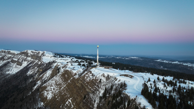 Aerial view of a solitary tower piercing the horizon atop the snow dusted Petit Mont Rond bathed in the soft glow of twilight Gex Auvergne Rh&ocirc;ne Alpes France.