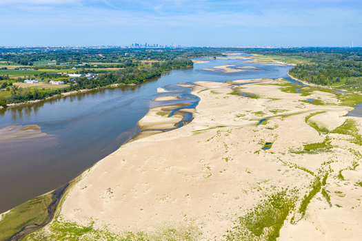 Aerial view of the Vistula river with low water levels and extensive exposed sandbanks under a clear blue sky with a distant city skyline in Poland.