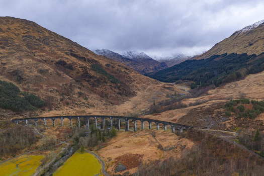 Aerial view of the Glenfinnan Viaduct with its curved concrete arches nestled in the rugged Scottish Highlands under an overcast sky Glenfinnan Scotland United Kingdom.
