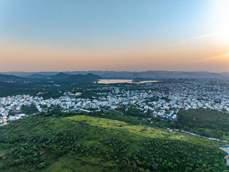 Aerial view of the city of Udaipur nestled among the Aravalli hills with a distant lake reflecting the golden sunset light in Udaipur Rajasthan India.