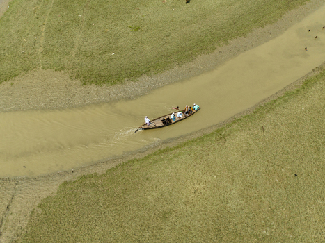 Aerial view of a boat glides through the muddy river contrasting with the verdant riverbanks Charmonai Barisal Division Bangladesh. Aerial view of a boat glides through the muddy river contrasting with the verdant riverbanks Charmonai Barisal Division Bangladesh.