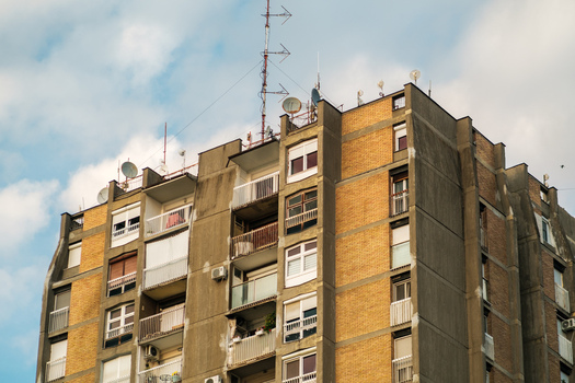 View of a residential apartment building with brick facade concrete balconies and numerous antennas against a blue sky in Novi Sad Vojvodina Serbia. View of a residential apartment building with brick facade concrete balconies and numerous antennas against a blue sky in Novi Sad Vojvodina Serbia.